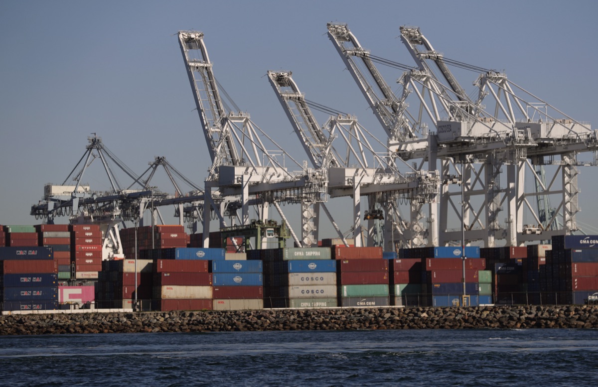 Ship-to-shore gantry cranes above stacked containers at the Port of Long Beach, seen from the water.