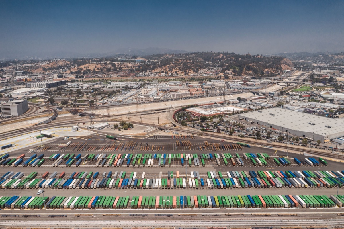 Rows of containers on chassis in a Los Angeles intermodal yard, with the freeway and hills beyond.